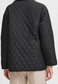 Sort quiltet jakke med diamantmønster, afslappet pasform og rundet kant. Fremstillet af let stof med sænkede skuldre og synlige syninger.