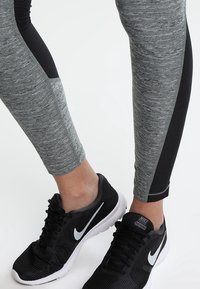 Leggings atletici grigi con un accento testurizzato nero, abbinati a scarpe da corsa nere con il logo swoosh bianco di Nike.