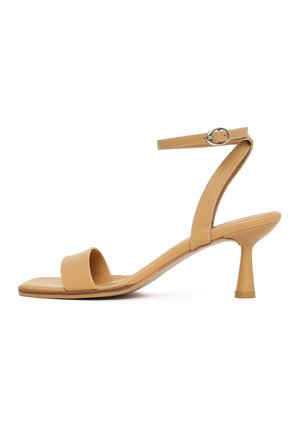 Sandale beige à bout ouvert avec un talon bas évasé et une fine bride de cheville maintenue par une boucle argentée.