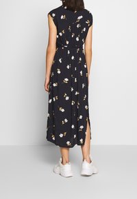 Blumen-Maxikleid mit kurzen Ärmeln, navyblauem Stoff, weißen und gelben Blumenmuster, seitlichen Schlitzen, kombiniert mit weißen Sneakers.