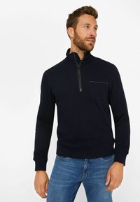 Dunkelblaues Pullover-Sweatshirt mit hohem Kragen, halbem Reißverschluss und kleiner Brusttasche. Hergestellt aus einem weichen, strukturierten Stoff.