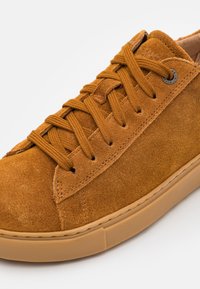 Barna velúr sneaker, kerek orral, lapos fűzőkkel és gumitalppal; öltögetett részletekkel és fém fűzőlyukakkal a fűző rögzítéséhez.