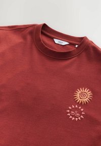 Bordový svetr s potiskem dvou slunečních motivů: jeden spirálový v béžové barvě, druhý geometrický s růžovými akcenty. Měkká tkanina a design s kulatým výstřihem.