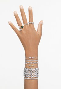 Smycken i silver med intrikata mönster. Distinkta ringar med gröna och klara stenar, samt flera armband med varierande texturer och accenter.