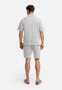 Kortærmet pyjamas sæt med krave i stribet grå stof, der har en løs pasform og matchende shorts. Glat tekstur og minimalistisk design.