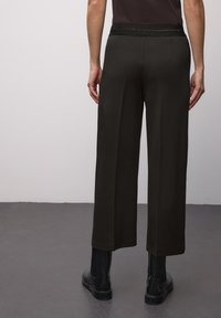 Pantaloni verdi scuro a gamba larga realizzati in tessuto morbido, con una cintura elastica nera in vita e due tasche posteriori. Abbinati a stivaletti neri alla caviglia.