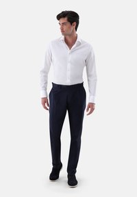 Dalla camicia bianca a maniche lunghe con sottili righe, abbinata a pantaloni su misura blu navy e scarpe nere. Linee pulite e design aderente.
