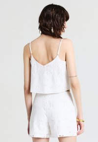 Set di top corto bianco e pantaloni corti con intricati ricami, motivi a giorno e spalline regolabili. Texture liscia e vestibilità comoda.