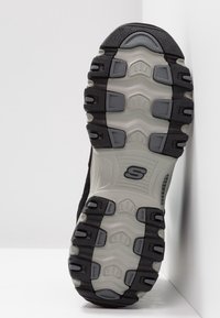 Podeszwa sportowych butów Skechers w czerni i szarości, charakteryzująca się strukturalną powierzchnią z wyraźnymi wzorami trakcjami oraz elastycznymi rowkami.