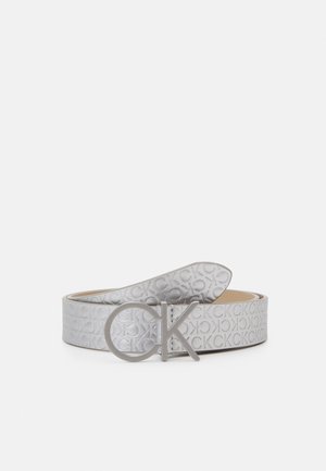 Zilveren Calvin Klein riem met reliëf van herhalend "CK" logo patroon en grote zilveren metalen gesp met "CK"-logo, opgerold op een witte achtergrond gelegd.