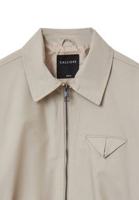 Beige Jacke mit Reißverschluss, spitzem Kragen und einer kleinen dreieckigen Tasche. Hergestellt aus glattem Stoff, mit feinen Nähten.