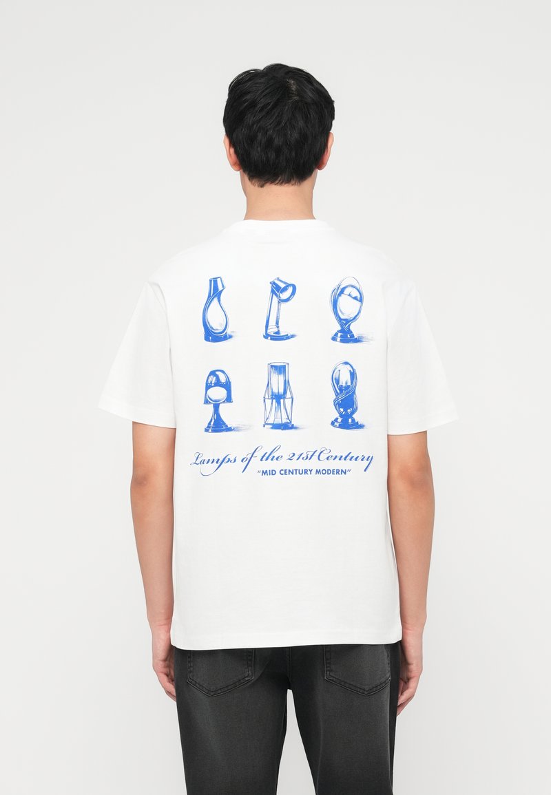 Άτομο που φοράει λευκό T-shirt με μπλε εικονογραφήσεις έξι μοντέρνων σχεδίων φωτιστικών και κείμενο "Φωτιστικά του 21ου Αιώνα 'Mid Century Modern'" στο πίσω μέρος.