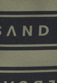 Olivų žaluma audinys su tekstūruota paviršiumi, kuriame yra ryškus juodas tipografija ir horizontaliu juostų raštu. Tekstas aiškiai rodo "SAND".