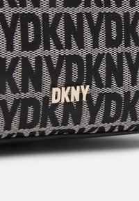Czarna i beżowa torba materiałowa z powtarzającym się wzorem logo „DKNY”, z błyszczącym złotym metalowym logo na przodzie. Teksturowane wykończenie.