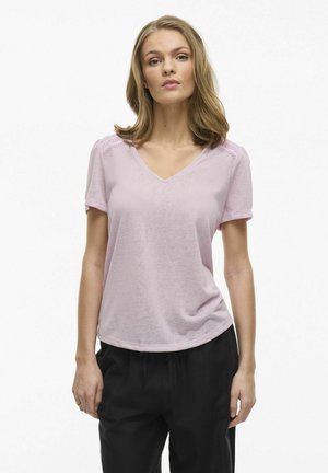 Camiseta de pico en rosa claro con mangas cortas, detalles de encaje en los hombros, combinada con pantalones negros; textura de tejido suave.
