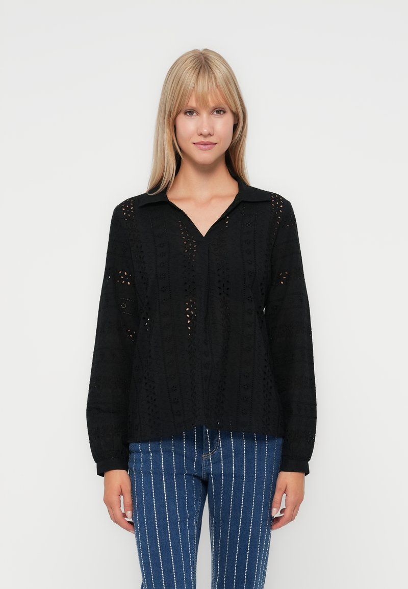 Black long-sleeve blouse with a collared neckline, featuring a textured pattern with cut-out details. Worn with striped jeans.
