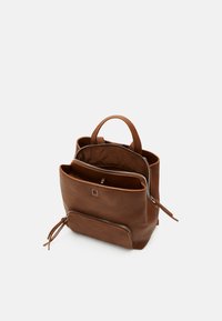 Mochila de cuero marrón con una forma rectangular estructurada. Presenta dobles cremalleras, asas superiores y un compartimento interno para organización.