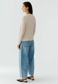 Hellrosa, gerippter Pullover mit langen Ärmeln, kombiniert mit lockeren blauen, hoch taillierten Jeans und schwarzen Slingback-Schuhen.