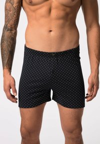 Pantalones cortos tipo bóxer en tela azul marino con lunares blancos, que presentan una cinturilla elástica y un cierre de botón en la parte frontal.