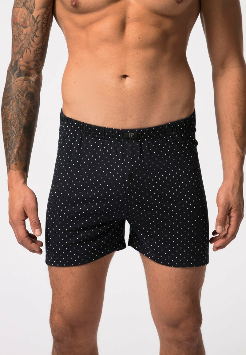 Pantalones cortos tipo bóxer en tela azul marino con lunares blancos, que presentan una cinturilla elástica y un cierre de botón en la parte frontal.