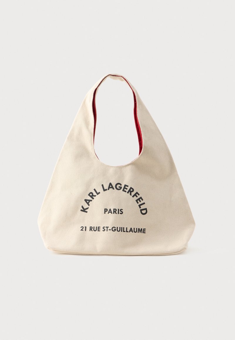 Sac cabas en tissu beige avec large anse, texte noir "Karl Lagerfeld Paris" et "21 Rue St-Guillaume" sur le devant, doublure rouge à l'intérieur de l'anse.