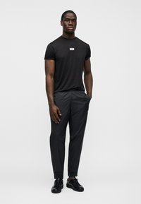 Μαύρο αθλητικό μπλουζάκι με κοντά μανίκια και λογότυπο· συνδυασμένο με μαύρο στενό παντελόνι με υφασμένο μοτίβο και αστραγάλους με μανσέτες.