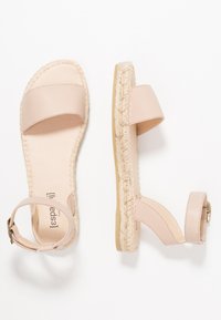 Beige flat sandals with wide front strap, ankle strap with buckle, and braided espadrille sole, shown from top and side views.