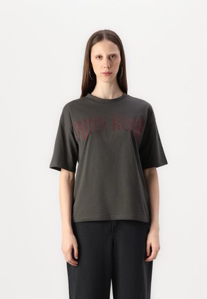 T-shirt en coton surdimensionné gris foncé avec des lettres rouges "PUNK ROCK". Manches courtes et design à col rond. Porté avec un pantalon noir ample.