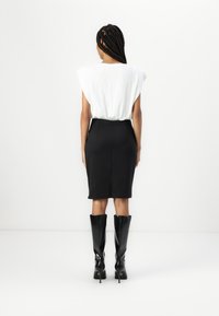 Jupe crayon noire associée à un chemisier blanc, avec des épaules structurées. Des bottes noires à talons montant jusqu'aux genoux complètent l'ensemble.