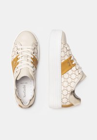 Sneaker con una base crema e accenti beige, tomaia in tessuto a motivo, suola in gomma bianca e dettagli metallici sul tallone.