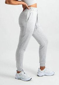 Jasnoszare dresy z elastycznym pasem, detal z sznurkiem, bocznymi kieszeniami oraz zwężanymi mankietami, w połączeniu z białymi sportowymi sneakersami.