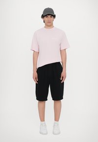 Light pink cotton t-shirt with short sleeves, paired with black knee-length shorts and white sneakers. A simple gray cap completes the look.