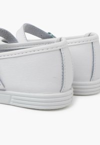 Weiße Lederschuhe mit einer glatten Textur, abgerundetem Absatz und dezenten Nähdetails. Die Sohle hat ein erhabenes, gerilltes Muster.