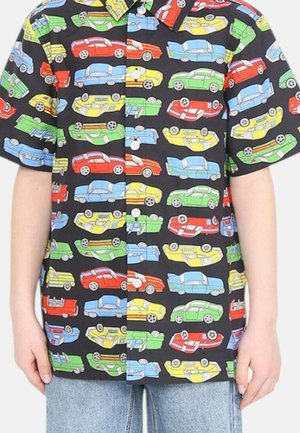 Czarna koszulka z krótkim rękawem z kolorowymi kreskówkowymi samochodami w czerwonych, niebieskich, żółtych i zielonych wzorach, noszona z jasnoniebieskimi dżinsami.
