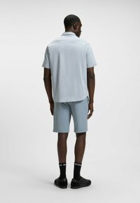 Light blue short-sleeve shirt with a collared neckline, paired with matching shorts. Black footwear and socks with white text.