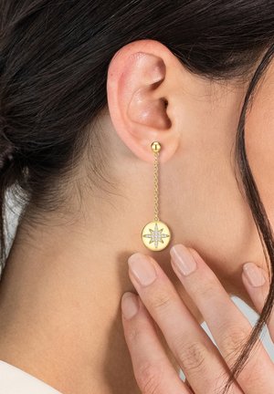 Cerceii de aur cu picătură prezintă un disc circular cu un design în formă de stea, suspendat de o lanț delicat de la un stud în formă de bilă.