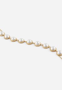 Collier en ton doré comportant huit perles rondes, chacune encadrée d'accents circulaires. De petites pierres à rhinestones bordent les maillons dorés, ajoutant de l'éclat.