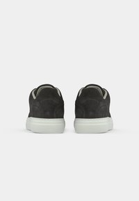 Par med svarte semskede sneakers med hvite gummisåler sett fra baksiden mot en ensfarget hvit bakgrunn.