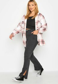 Koszula w kratę w różowo-białe wzory, czarny top na ramiączkach, ciemnoszare jeansy z wysokim stanem z bocznymi rozcięciami oraz czarne sneakersy typu high-top.