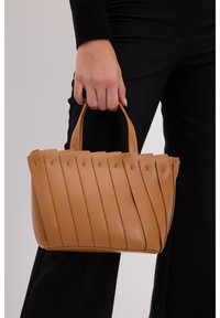 Sac à main en cuir tan avec un design plissé, deux courtes poignées et une texture lisse. Construction robuste avec des coutures régulièrement espacées.