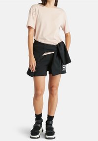 T-shirt en coton rose clair associé à un short en coton noir. Sweatshirt noir noué autour de la taille et sandales noires épaisses avec des brides.