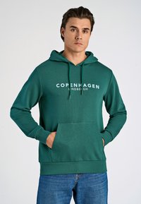 Felpa verde con cappuccio e tasca a marsupio, con la scritta "Copenhagen Lindbergh" stampata in bianco. Tessuto liscio, cordini regolabili, polsini a costine.
