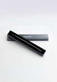 Silverkedja armband visat i en svart, vadderad låda med en logotyp. Armbandet har ovala länkar och ett lås för stängning.