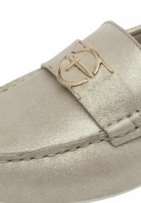 Metalliikuldne loafers tekstuuriga ülemise osaga, mis sisaldab silmapaistvat kuldse tooni logo aktsenti rihmal ja tikitud detailide lõigetel.