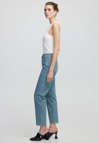Vaqueros de cintura alta en un azul claro con un corte relajado, que presentan un diseño clásico de cinco bolsillos. Combinados con una camiseta sin mangas blanca y mule de tacón negro.