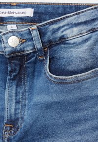 Jeans Calvin Klein, talla 8, hechos de denim azul. Cuenta con un bolsillo delantero, botón plateado con el logo "CK" y detalles de costura visibles.