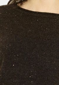 Gros plan sur un pull en maille brun foncé avec de petits sequins brillants dispersés sur le tissu au niveau de la partie supérieure de la poitrine et de l'épaule d'une personne.