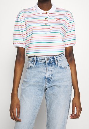 Personne portant un polo blanc avec des rayures horizontales multicolores et le logo Nike, associé à un jean en denim bleu clair taille haute.