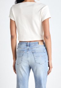 Biała prążkowana bluzka crop top z krótkimi rękawami, w zestawie z jasnoniebieskimi dżinsami z tylnymi kieszeniami i metką marki na pasku.