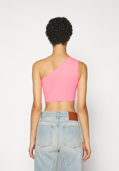 Rosa kort tanktopp med én skulderstropp, paret med lyseblå høytlivsjeans med et lærmerke bak.